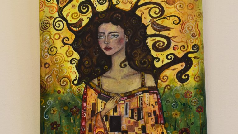 Młoda, długowłosa kobieta enface na tle rozkwieconej łąki. Zamiast nieba widzimy żółte tło - jakby ogromne słońce. Rozwiane włosy kobiety tworzące ornamentalne zawijasy spowijają tło. W ich segmentach widać dwa ptaki. Szata kobiety przypomina misterną sie