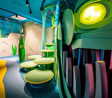 Kolorowa sala edukacyjno-zabawowa inspirowana podwodnym światem, z ilustracjami ryb na ścianach, interaktywnymi ekranami i miękkimi elementami do zabawy.