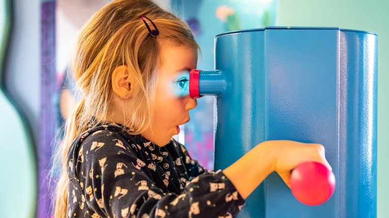 Dziecko korzystające z interaktywnego stanowiska edukacyjnego, zaglądające przez wizjer i obracające elementem urządzenia.